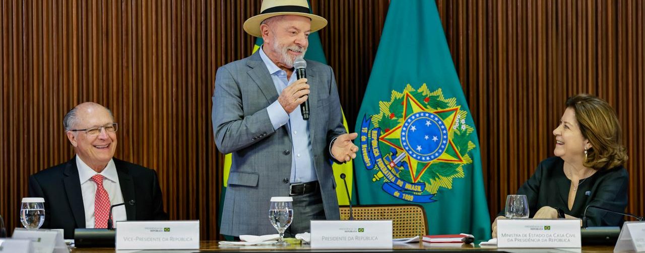 Presidente Lula durante evento em que foram anunciadas as medidas de proteção e prevenção aos efeitos do El Niño, em pé, atrás de uma mesa, com Geraldo Alckmin sentado à esquerda de quem vê e Mirian Belchior à direita