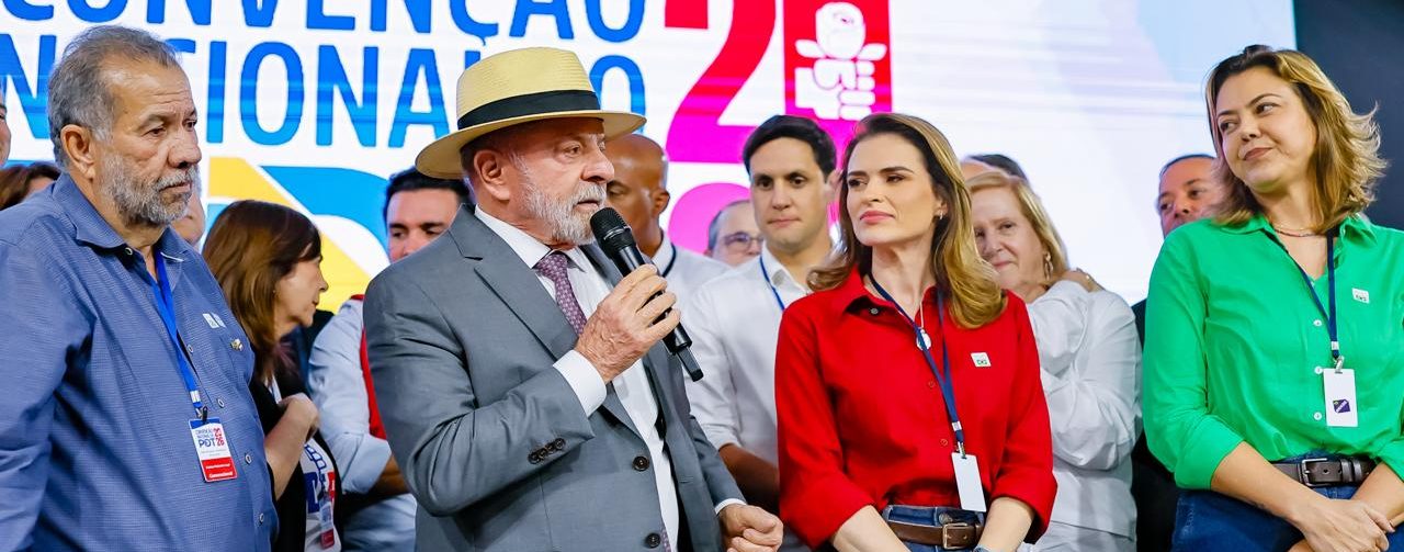 Presidente Lula, em pé, com microfone na mão, uma mesa na frente e vários representantes do PDT ao lado.