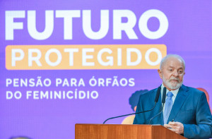O presidente Lula fala num púlpito durante evento no Palácio do Planalto. Ao fundo, um painel com o título Futuro Protegido, relativo ao evento para sancionar lei sobre pensão para órfãos de feminicídio