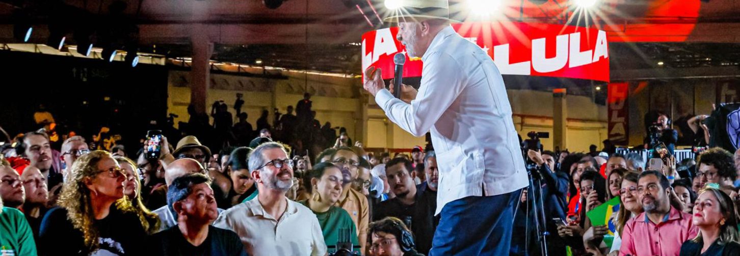 Presidente de lado, com chapéu e camisa branca, inclinado para a frente falando com a plateia