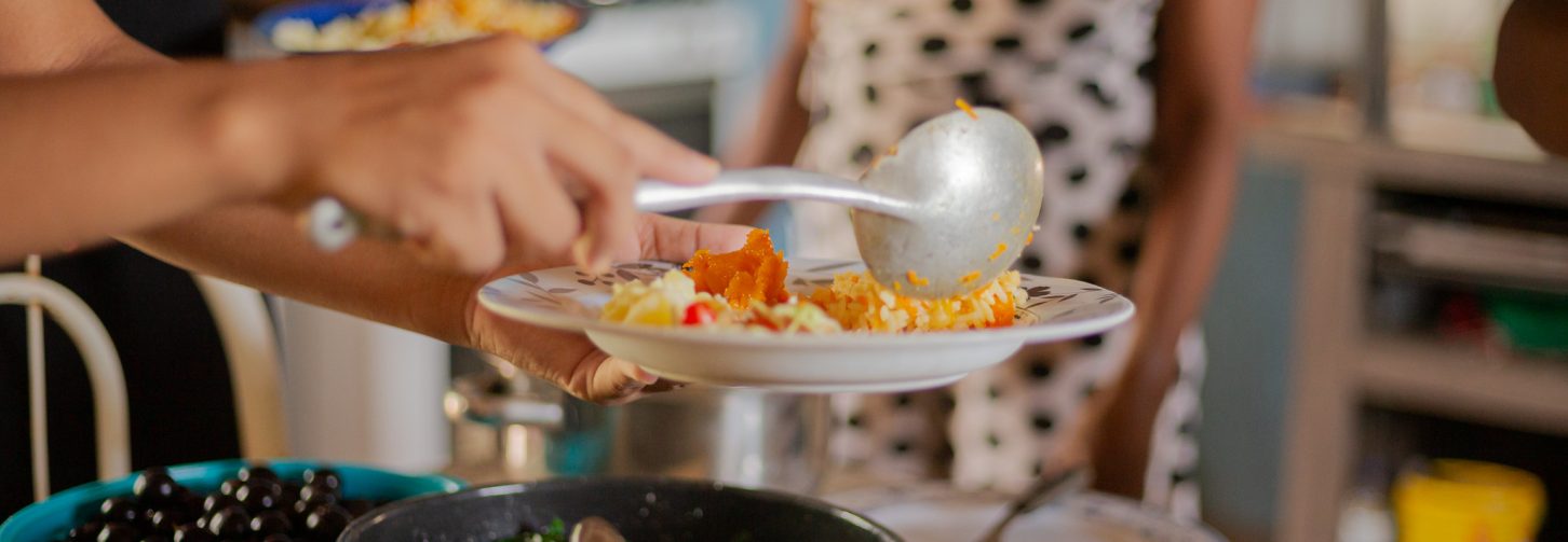 Um ´prato de comida com ingredientes bem variados sendo servido ao lado de panelas