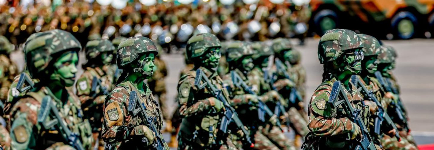 Mulheres soldado desfilam marchando com caras pintadas de verde e preto e armas em punho