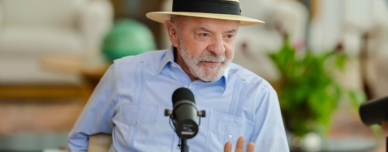 Lula, sentado, veste camisa azul claro e chapéu Panamá
