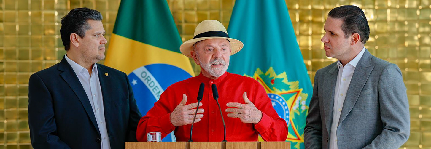 Davi Alcolumbre, Lula e Hugo Motta dando entrevista à imprensa após almoço no Palácio da Alvorada. Ao fundo, a bandeira do Brasil e o brasão da República