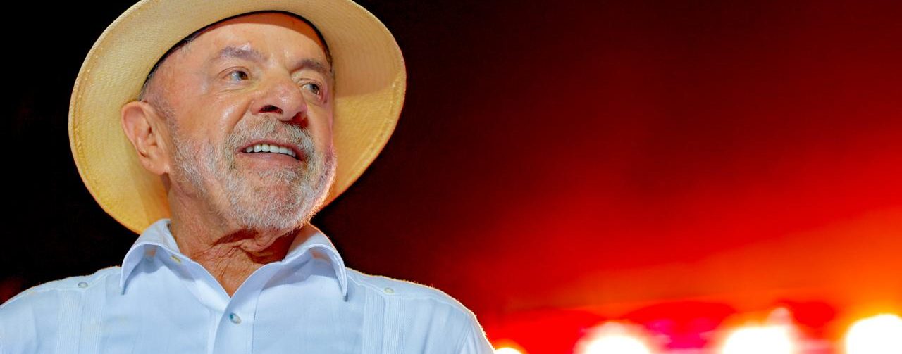 Presidente Lula em primeiro plano com um fundo avermelhado desfocado durante evento de campanha em Natal (RN)