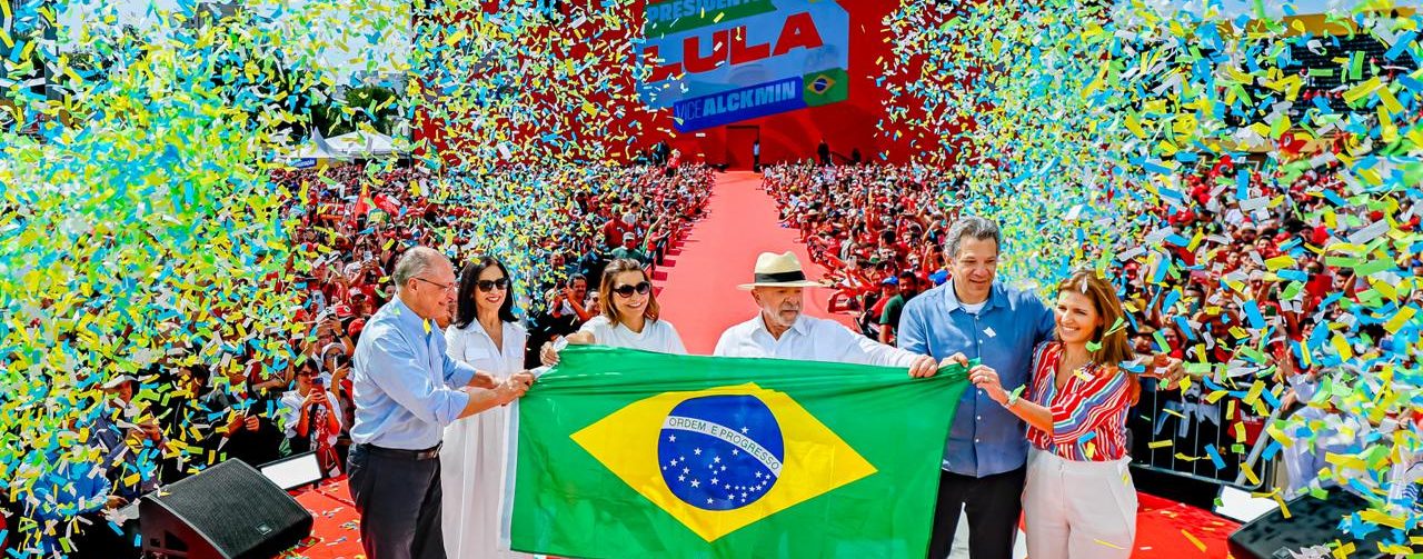 Alckmin, Janja, Lula e Lu Alckmin seguram bandeira do Brasil em meio a muitos papéis picados no fim do evento na Vila Euclides