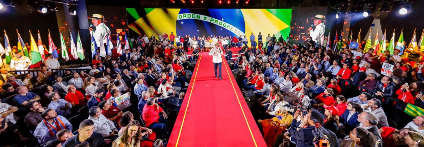 Lula caminha sobre palanque vermelho, com microfone em punho, discursando para plateia em volta