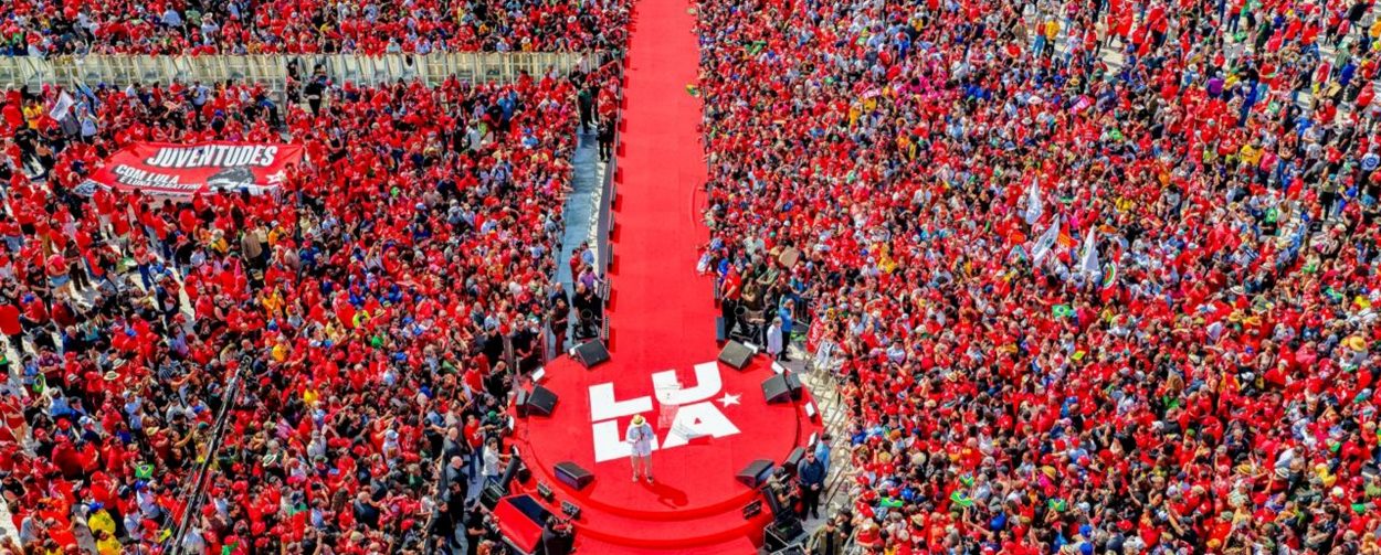Imagem aérea mostra o estádio da Vila Euclides lotado, com uma passarela ao meio e o presidente Lula falando na ponta de baixo do enquadramento