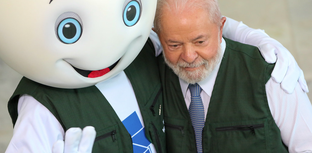 O presidente Lula com o jaleco do programa Mais Médicos abraçado com o Zé Gotinha
