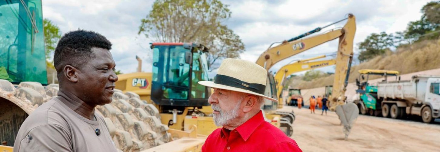 Presidente Lula cumprimenta trabalhador num canteiro de obras, em meio a grandes tratores numa rodovia